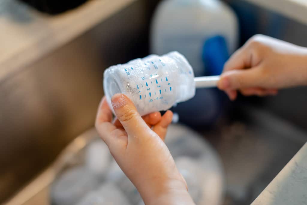 Eine Mutter reinigt das Babyfläschchen mit einer Bürste