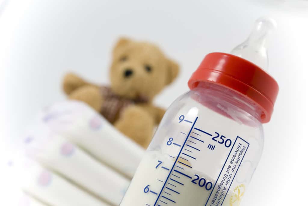 Babyflasche 50 Ein Stapel Windeln, Babyflasche und ein Teddybär vor weißem Hintergrund