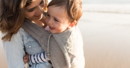 Mutter mit Babybauchtrag am Strand