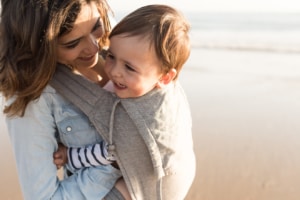 Mutter mit Babybauchtrag am Strand