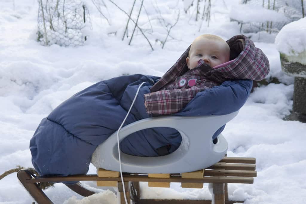 Baby im Schneeanzug sitzt auf einem Schlitten im Schnee